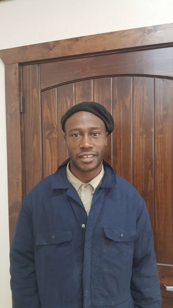 Man smiling in a blue work jacket standing in front of a wooden door, representing success stories from VIP Staffing and the positive impact of their employment services.