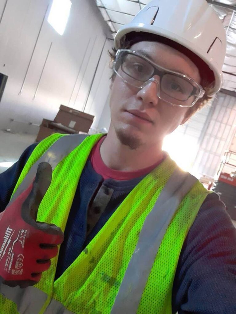 Young man in safety gear, wearing a hard hat and safety glasses, giving a thumbs up in a construction environment, representing success in job placement through VIP Staffing.