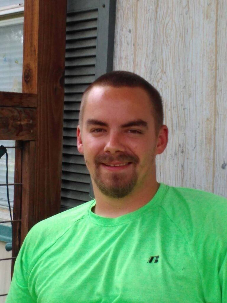 Smiling man in a bright green shirt, sitting outdoors, representing success stories of individuals aided by VIP Staffing in their career journeys.
